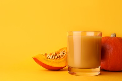 Photo of Tasty pumpkin juice in glass, whole and cut pumpkins on orange background. Space for text