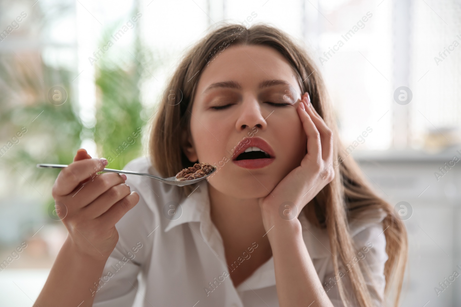 Photo of Sleepy young woman eating breakfast at home in morning