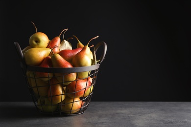 Photo of Basket with ripe pears on table against black background. Space for text