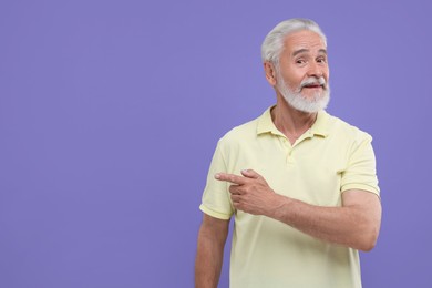Photo of Special promotion. Senior man pointing at something on purple background. Space for text