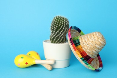 Photo of Mexican sombrero hat, cactus and maracas on light blue background