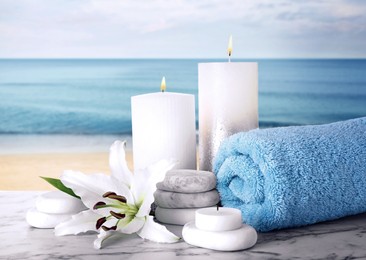 Image of Composition with towel, spa stones and candles on marble table against seascape
