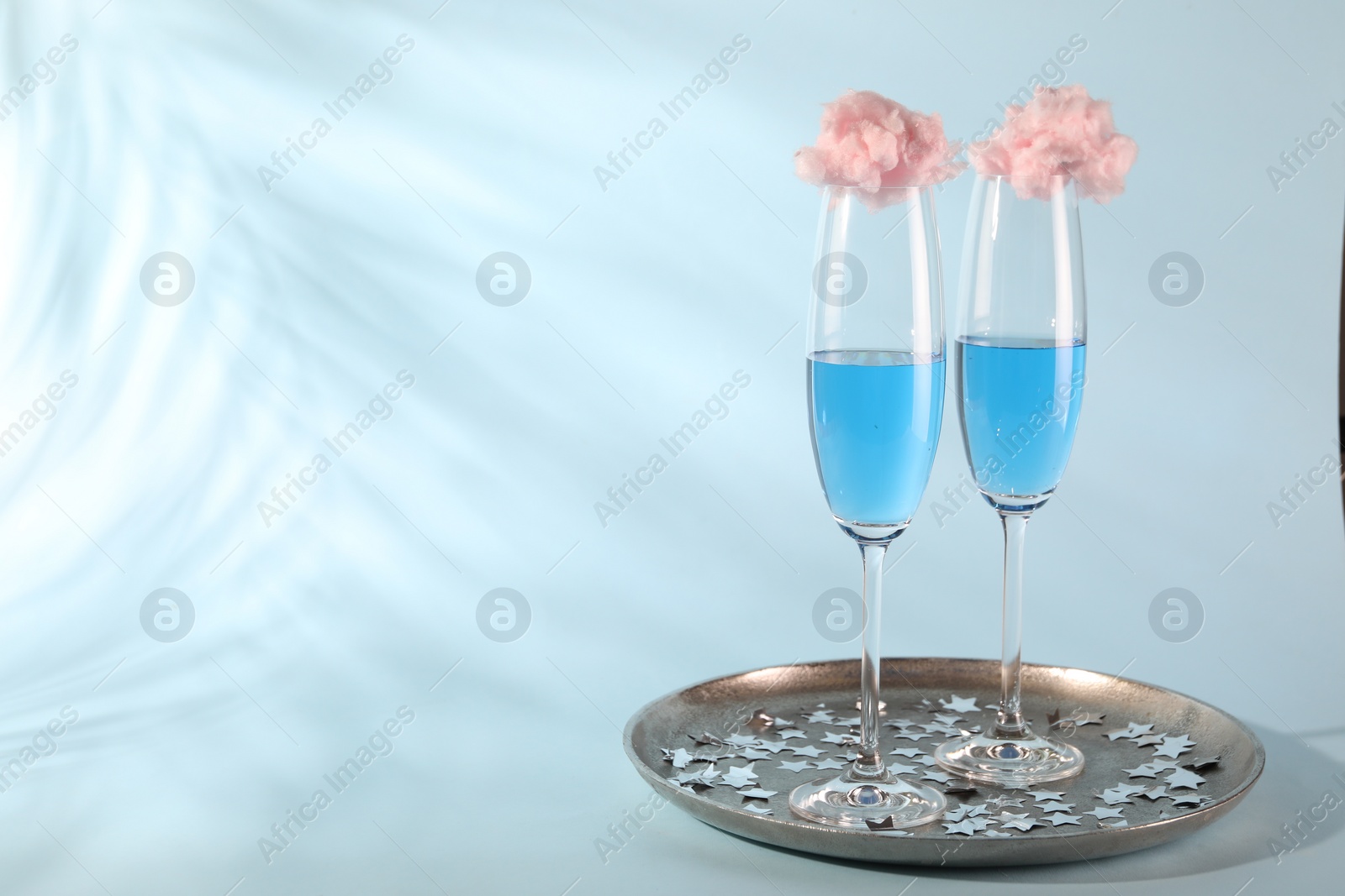 Photo of Cotton candy cocktails in glasses and confetti on light blue background, space for text
