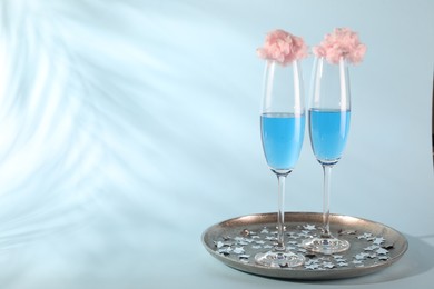 Photo of Cotton candy cocktails in glasses and confetti on light blue background, space for text
