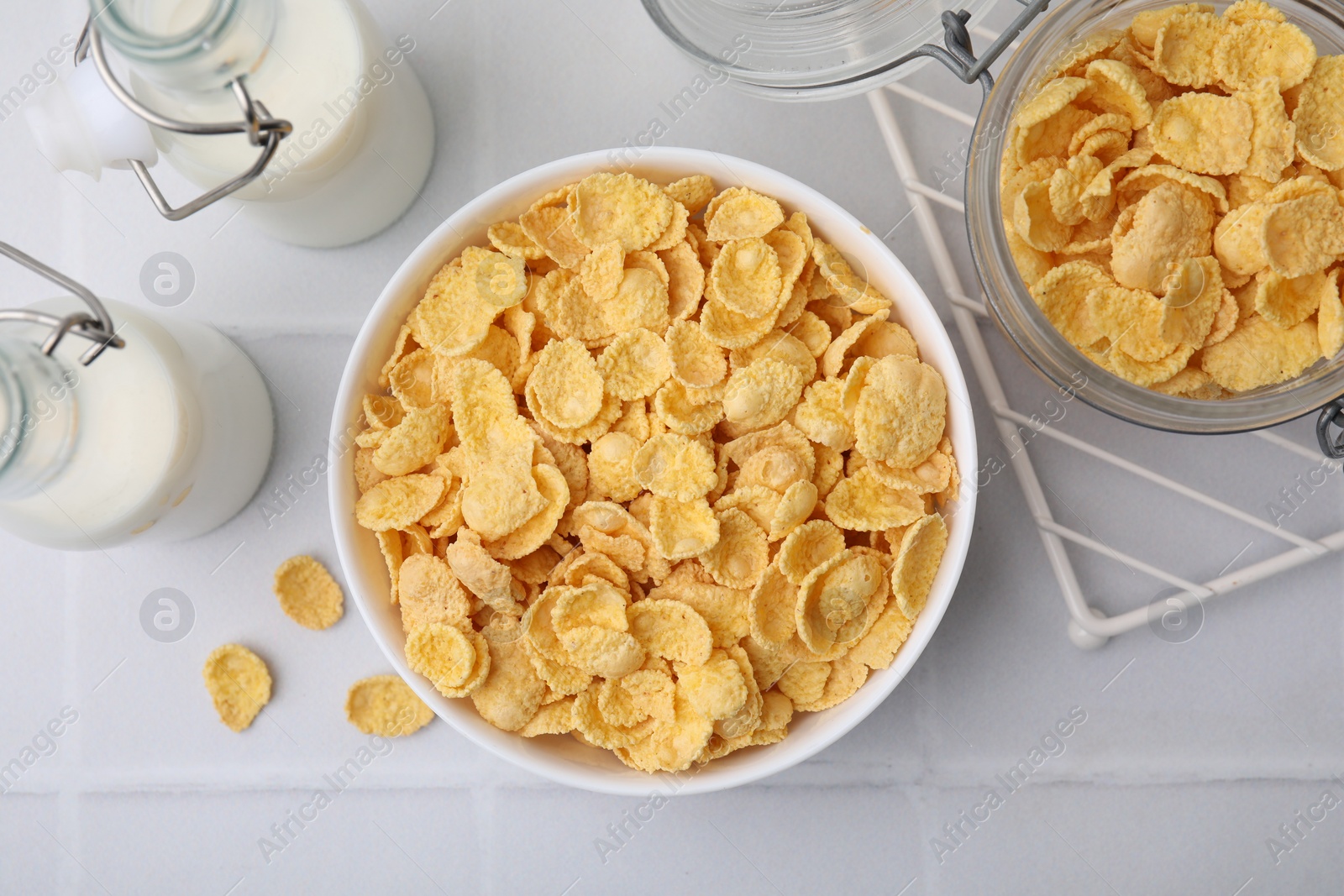 Photo of Tasty crispy corn flakes and milk on white tiled table, flat lay. Breakfast cereal