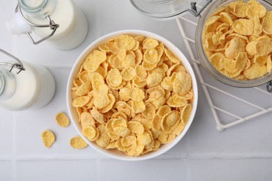 Photo of Tasty crispy corn flakes and milk on white tiled table, flat lay. Breakfast cereal