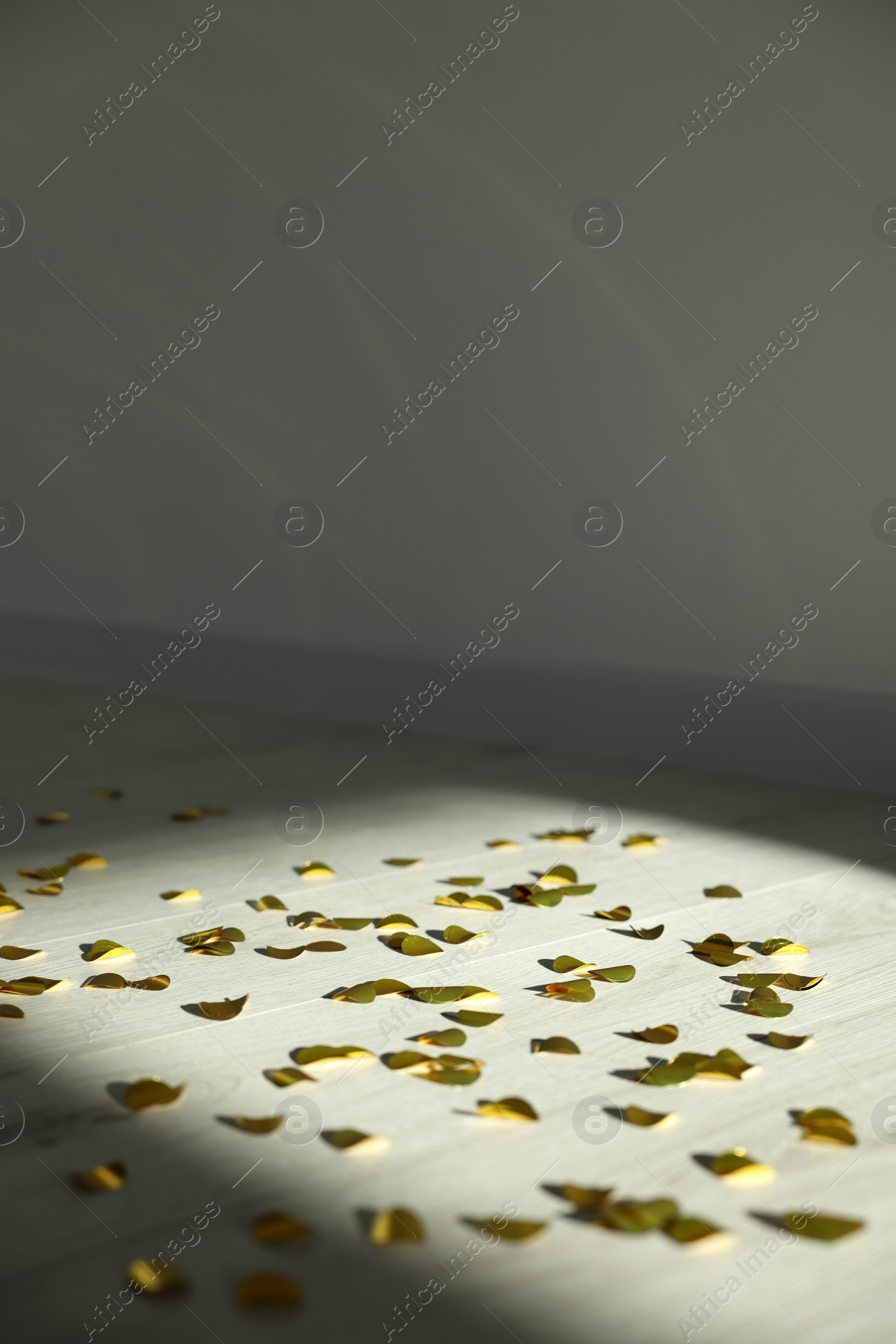 Photo of Beautiful confetti under spotlight on wooden floor indoors. Space for text