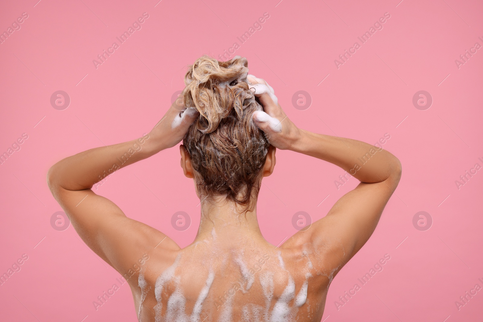 Photo of Woman washing hair on pink background, back view