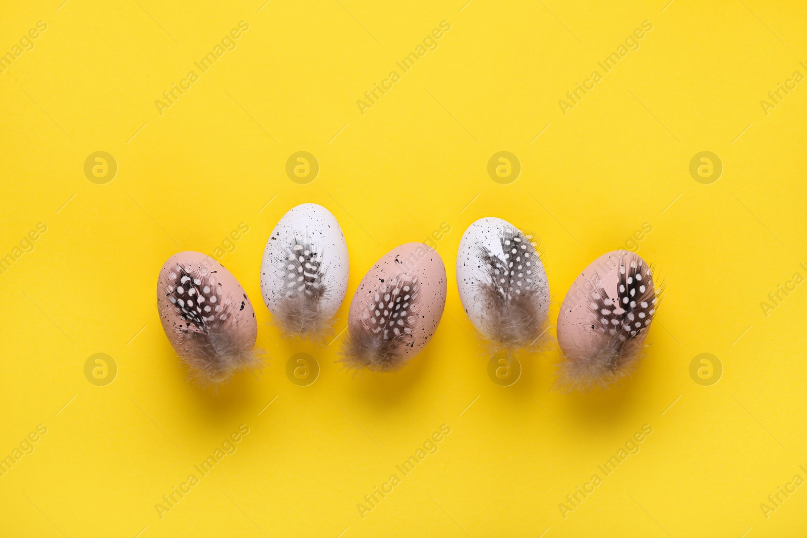 Photo of Many painted Easter eggs with feathers on yellow background, flat lay
