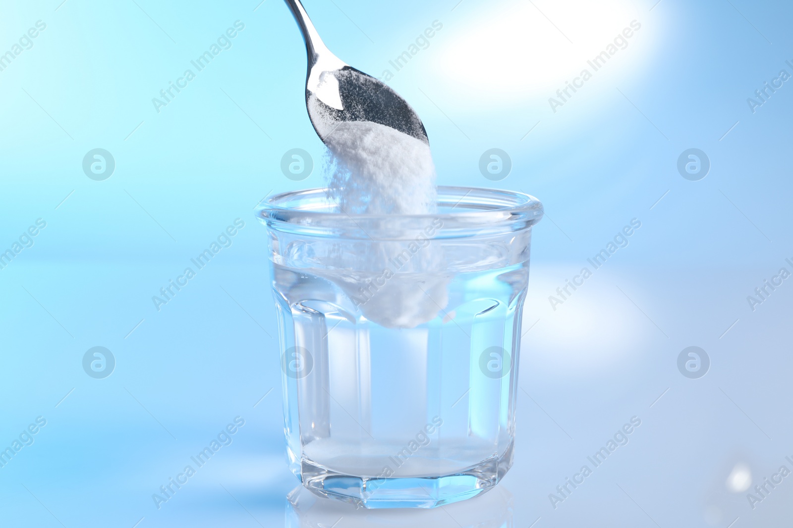 Photo of Adding baking soda into glass of water on light blue background