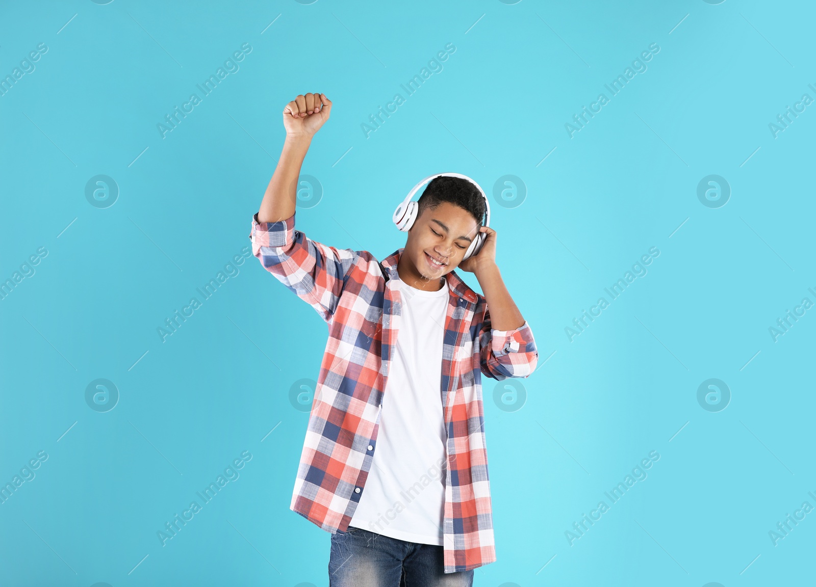 Photo of African-American teenage boy listening to music with headphones on color background