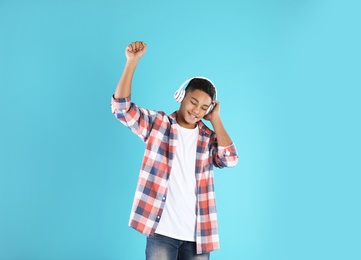 African-American teenage boy listening to music with headphones on color background