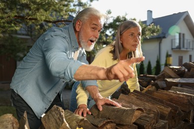 Photo of Concept of private life. Curious senior couple spying on neighbours over firewood outdoors