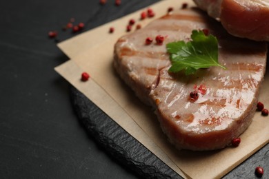 Delicious tuna steak with parsley and spices on black table, closeup. Space for text