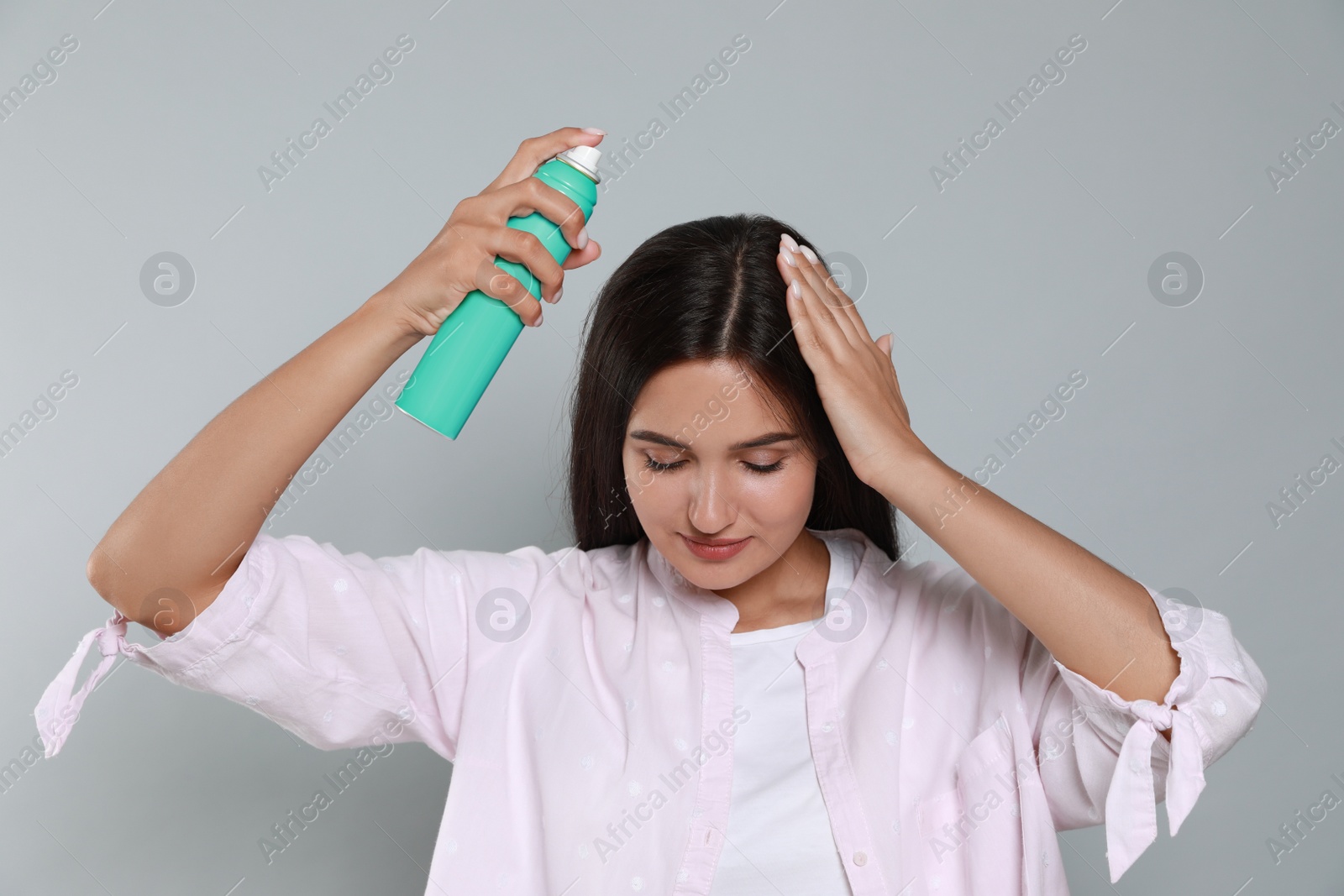 Photo of Woman applying dry shampoo onto her hair on light grey background