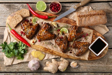 Tasty chicken wings glazed in soy sauce with garnish on wooden table, flat lay