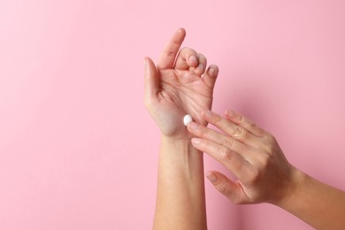 Photo of Woman applying cosmetic cream onto hand on pink background, top view. Space for text