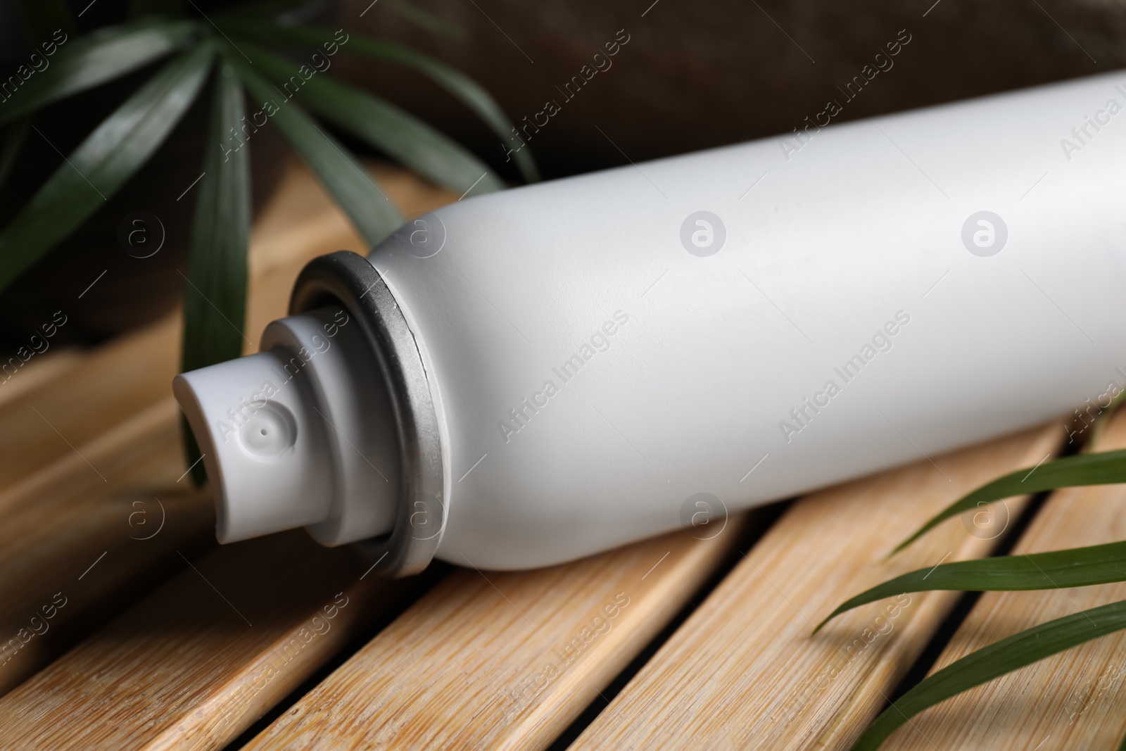 Photo of Dry shampoo spray and green leaves on wooden table, closeup