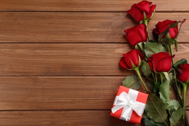 Photo of Beautiful red roses and gift box on wooden background, flat lay with space for text. Valentine's Day celebration