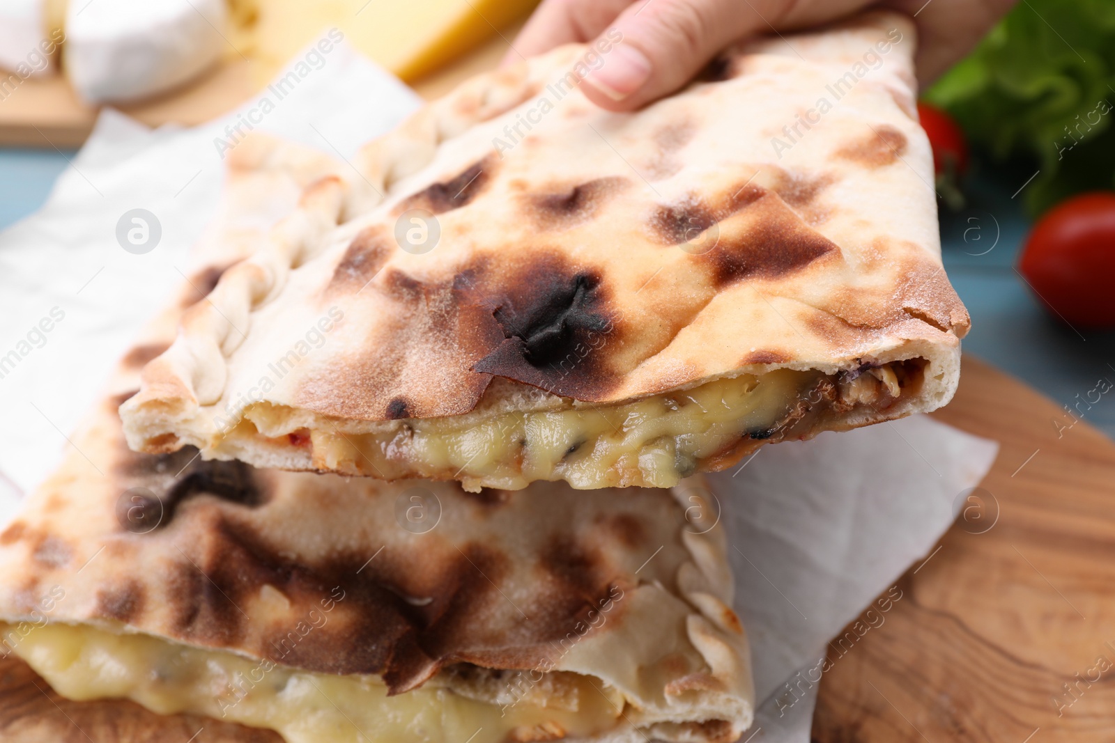 Photo of Woman holding tasty pizza calzone with cheese at table, closeup