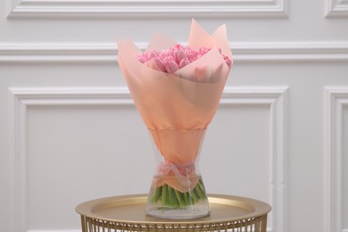 Bouquet of beautiful pink tulips in vase on table near white wall