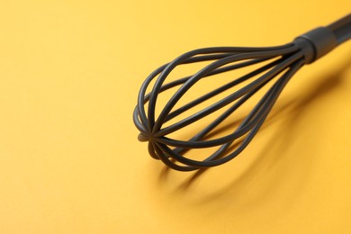 Plastic whisk on yellow background, closeup. Space for text