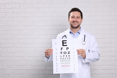 Ophthalmologist with vision test chart near white brick wall, space for text
