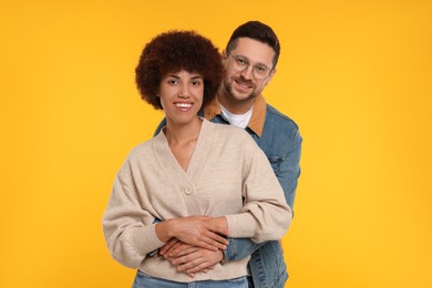 Photo of International dating. Happy couple hugging on orange background,