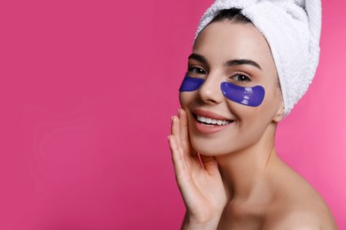 Photo of Beautiful young woman with under eye patches and hair wrapped in towel on pink background, space for text