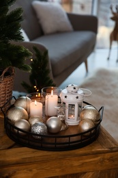 Burning candles, lantern and Christmas balls on wooden table indoors