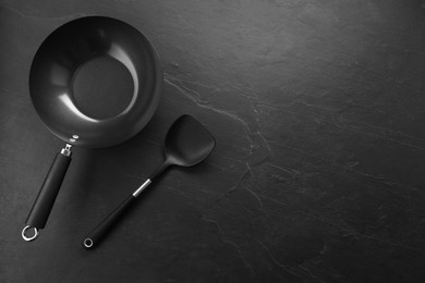 Photo of Black metal wok and spatula on dark textured table, top view. Space for text