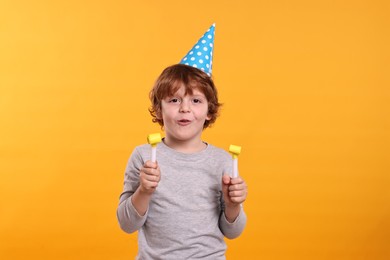 Photo of Birthday celebration. Cute little boy in party hat with blowers on orange background