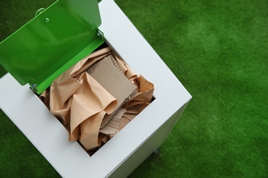 Trash bin with paper and cardboard on color background, space for text. Recycling concept