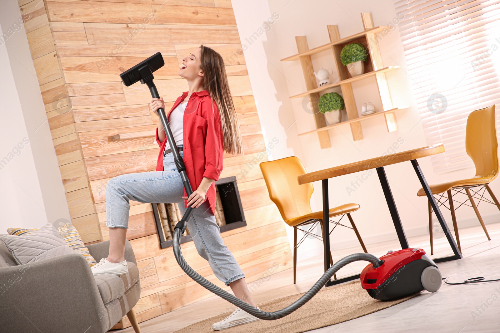 Photo of Young woman having fun while vacuuming at home