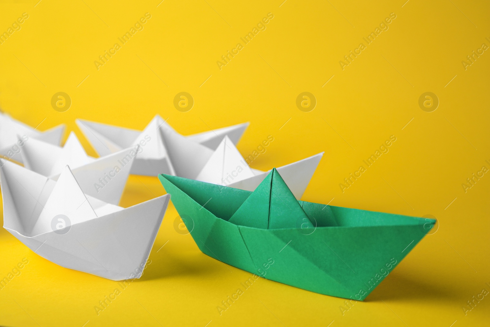 Photo of Group of paper boats following green one on yellow background. Leadership concept