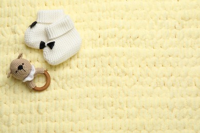 Cute baby booties and toy on yellow knitted fabric, flat lay. Space for text