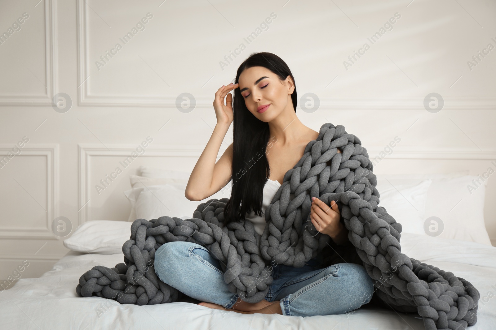 Photo of Young woman with chunky knit blanket on bed at home