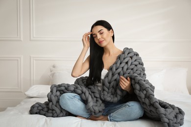 Young woman with chunky knit blanket on bed at home