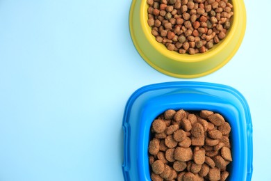 Photo of Dry pet food in feeding bowls on light blue background, flat lay. Space for text