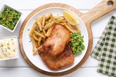 Photo of Tasty fish, chips, sauce, peas and lemon on white wooden table, top view