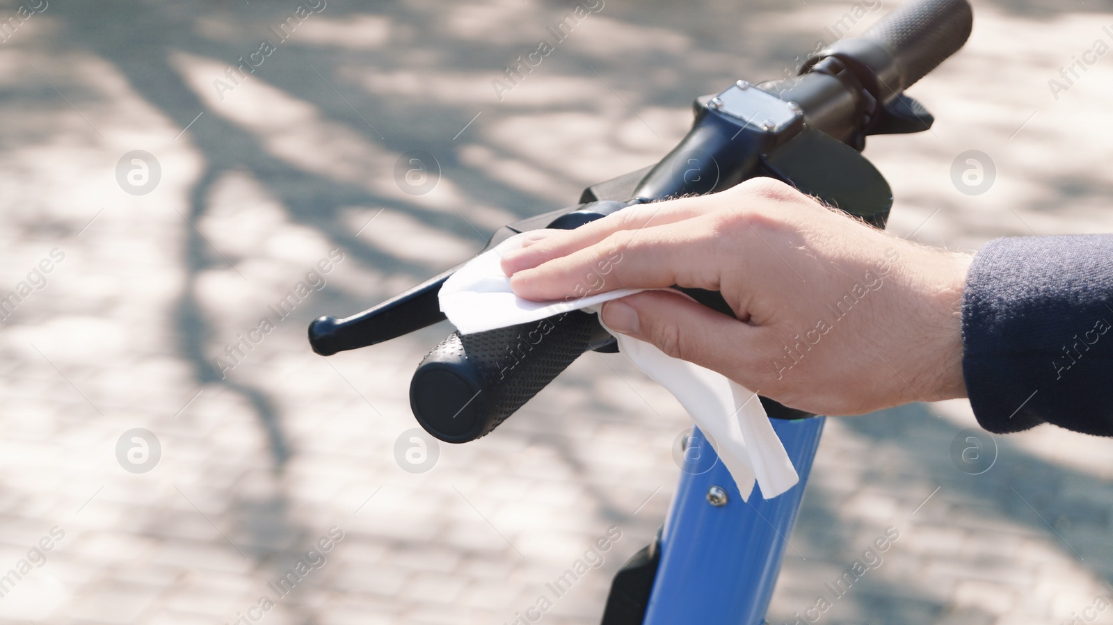 Photo of Man cleaning scooter steering wheel with wet wipe outdoors, closeup. Protective measures