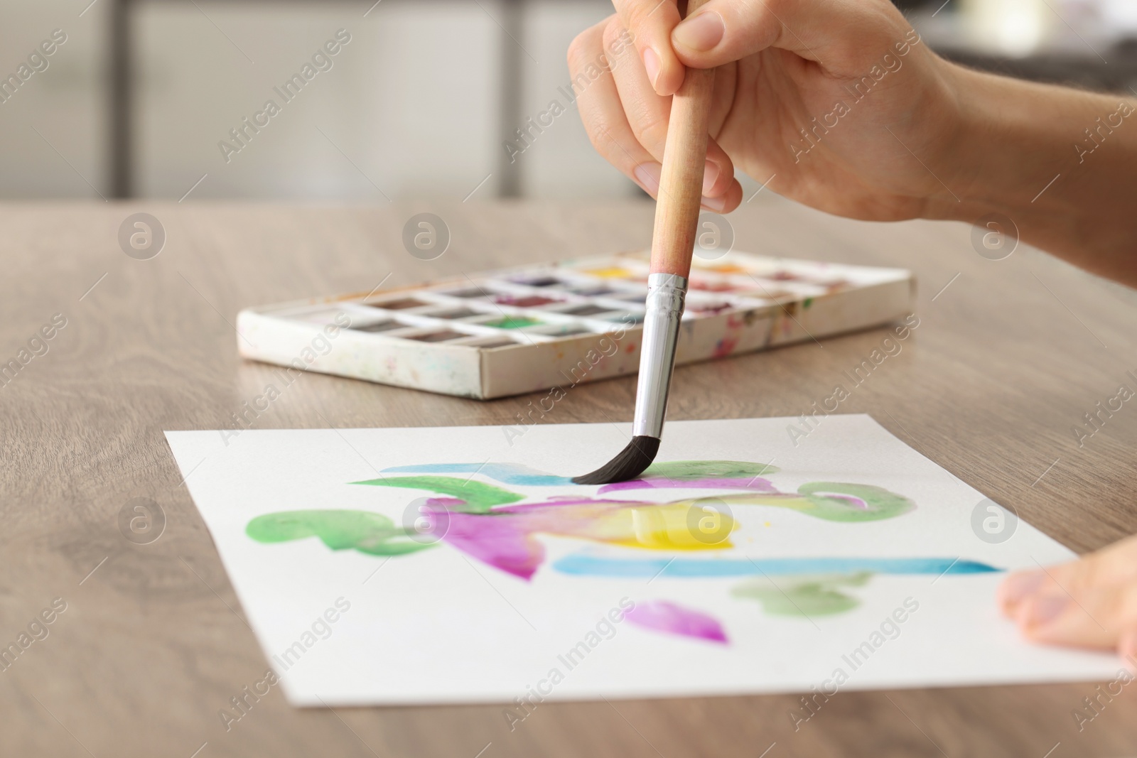 Photo of Woman painting with watercolor at wooden table, closeup