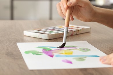 Photo of Woman painting with watercolor at wooden table, closeup