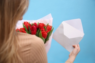 Photo of Woman holding envelope with blank greeting card and bouquet of tulips on turquoise background, closeup