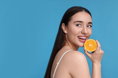 Photo of Beautiful young woman with piece of orange on light blue background. Space for text