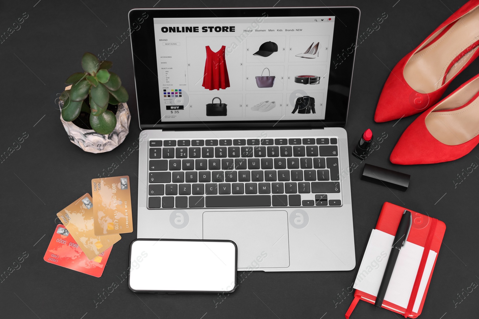 Photo of Online store website on laptop screen. Computer, smartphone, credit cards, women's shoes, stationery and lipstick on black background, above view