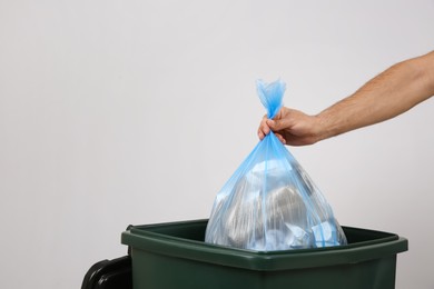 Photo of Man throwing garbage bag into bin on light background, closeup. Space for text