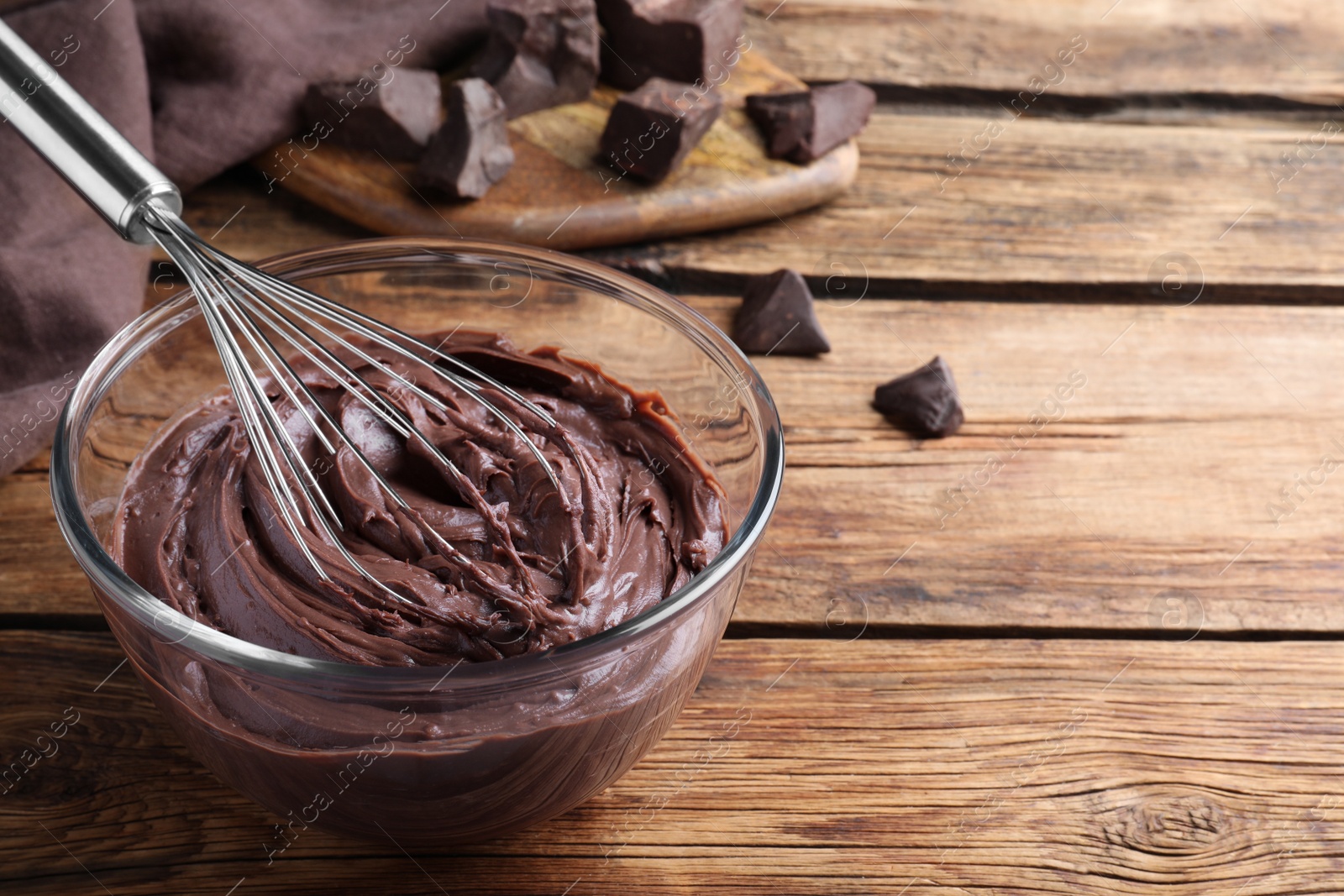 Photo of Whipping chocolate cream with balloon whisk on wooden table. Space for text