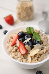 Photo of Tasty oatmeal with strawberries, blueberries and almond petals in bowl on white wooden table