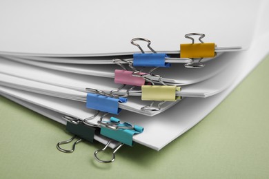 Photo of Sheets of paper with clips on light green background, closeup